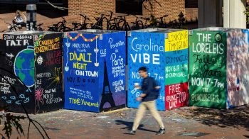 Student walking on brick pathways by murals advertising student groups on the campus of UNC-Chapel Hill.