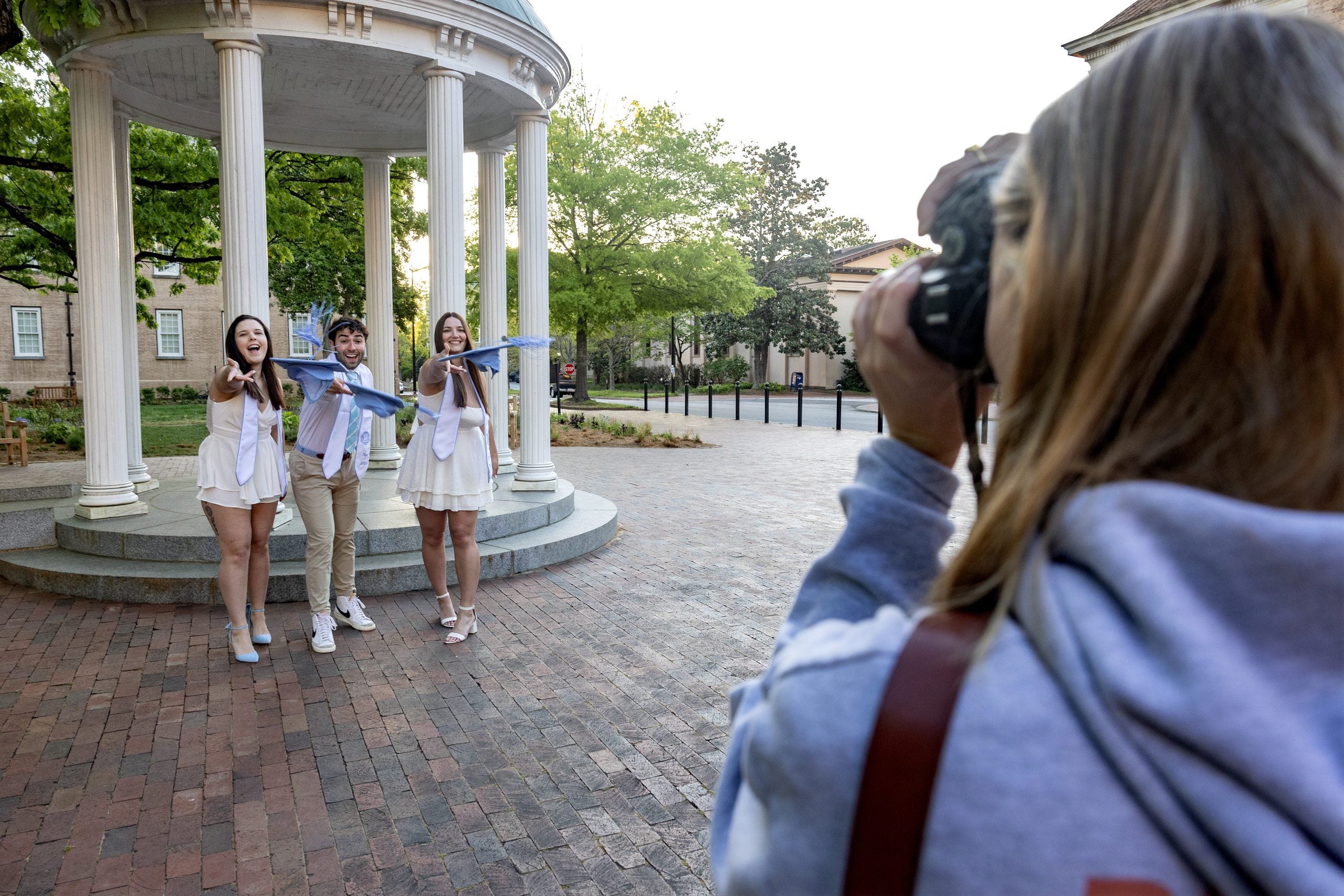 Photographer Samantha Lewis making a photo of Brittany Harrelson, Nick Clementi, and Shaena Riddles getting ready to toss their graduation caps in front of the Old Well on the campus of UNC-Chapel Hill.