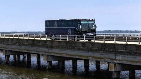 Navy blue Tar Heel Bus Tour bus driving over a bridge over a waterway.
