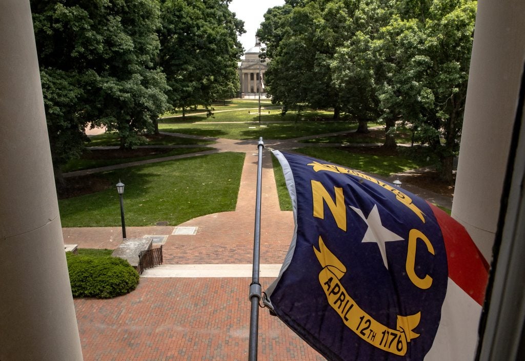 North Carolina state flag flying from the the exterior of South Building on the campus of UNC-Chapel Hill. Polk Place, known colloquially as the Quad, is seen in the background.