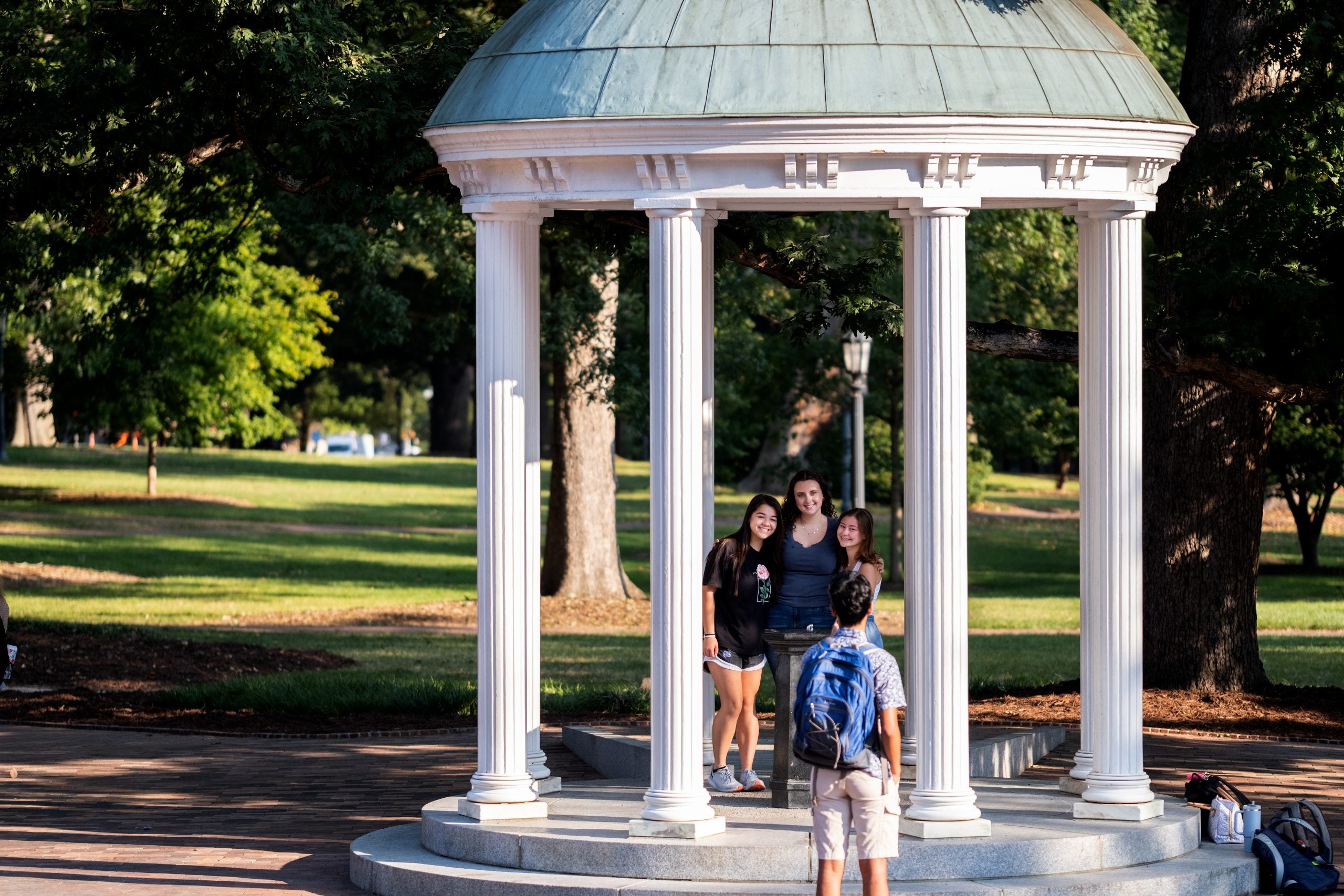 Three students posing for a photo in front of the fountain of the Old Well as another person takes their picture.