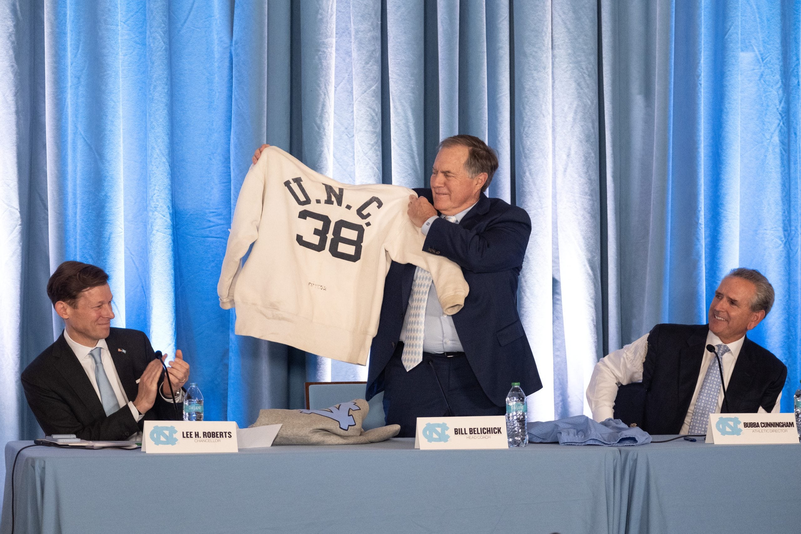 Bill Belichick holds up his father's U.N.C. sweatshirt during a press conference with Chancellor Lee H. Roberts and Athletic Director Bubba Cunningham.