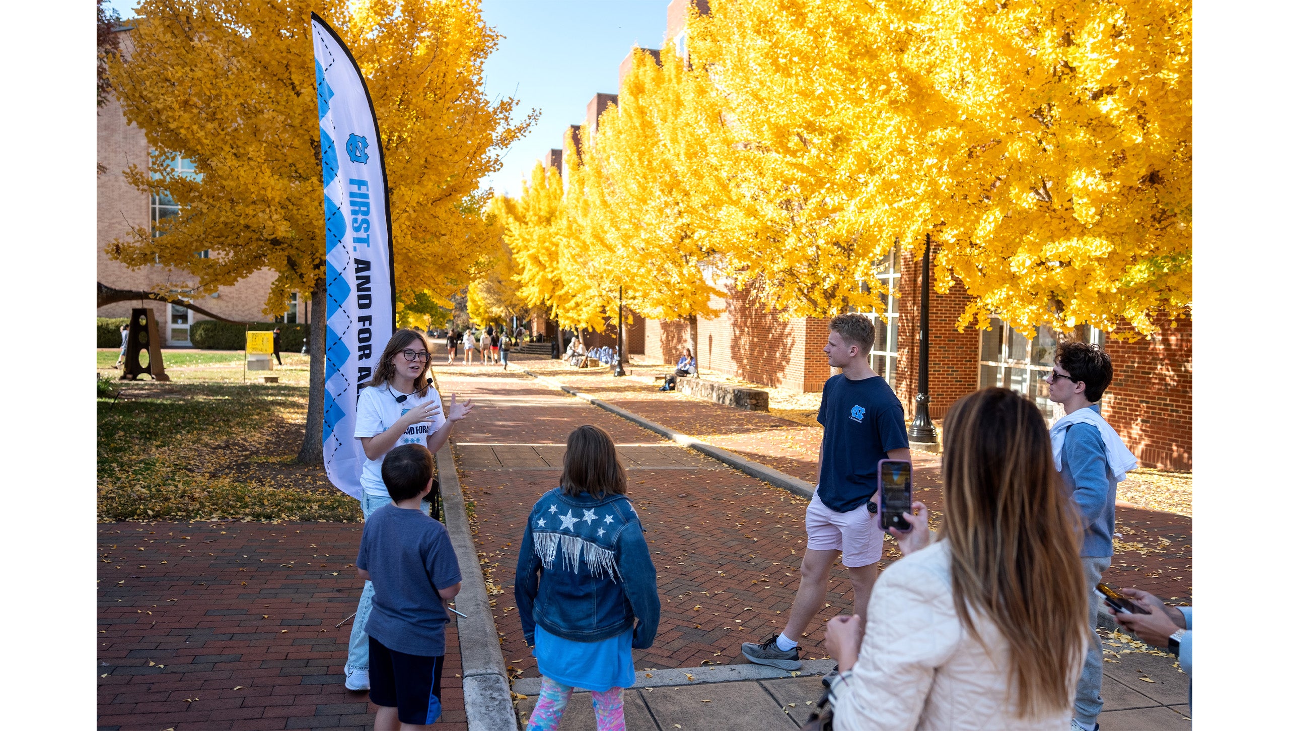 A UNC Visitors Center tour guide speaking to campus visitors near rows of yellow Ginkgo trees.