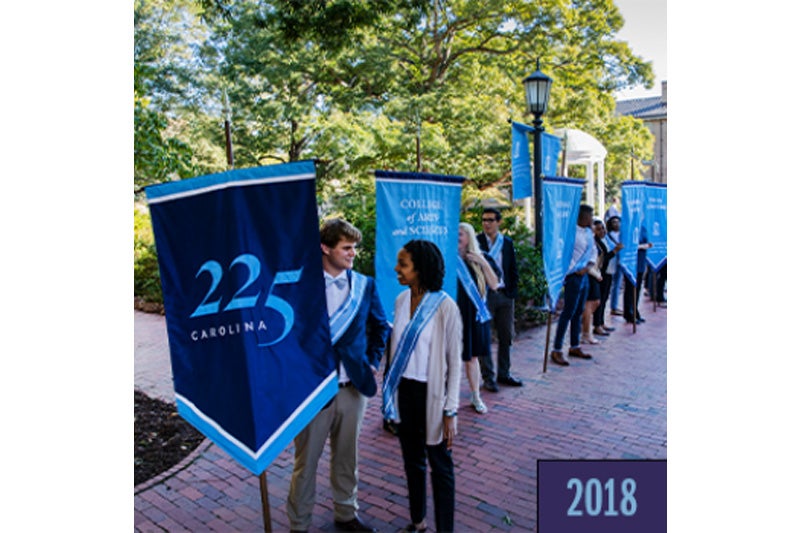 A row of people holding UNC-Chapel Hill-themed banners during a University Day event. Prominently featured are a man and a woman talking, standing next to a banner that reads 