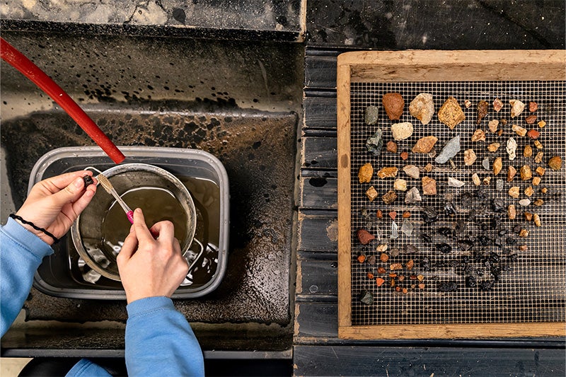 Hands of a student seen cleaning and sorting through artifacts in a lab.