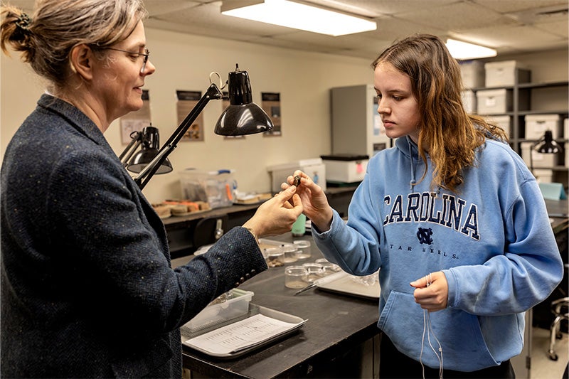 A professor and student holding and talking about excavated artifacts in a lab.