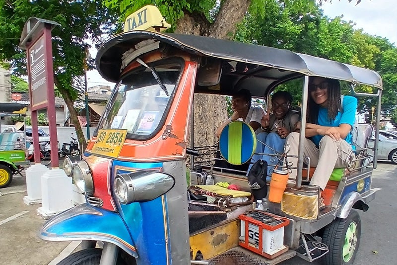 Aiden Bryant and two other students in the back row of seating of an open-air taxi in Thailand.