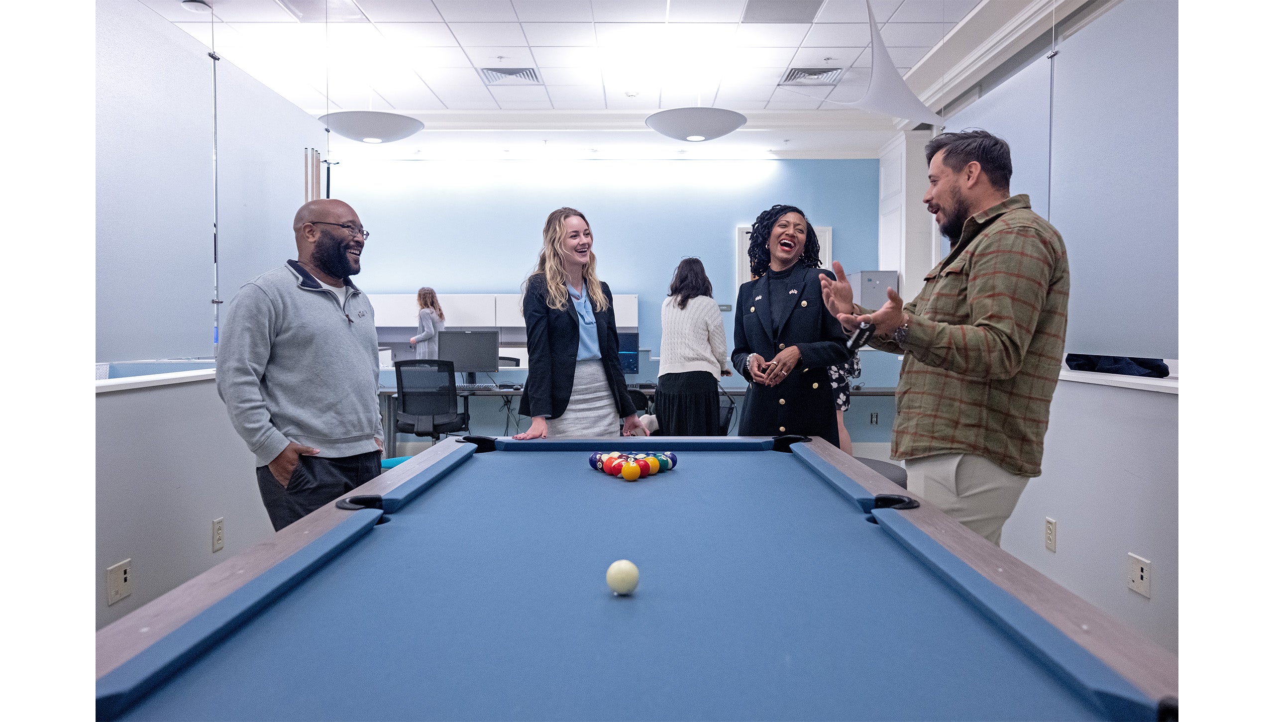Four people laughing and talking by a pool table inside the Military and Veteran Student Success Center on the campus of UNC-Chapel Hill.