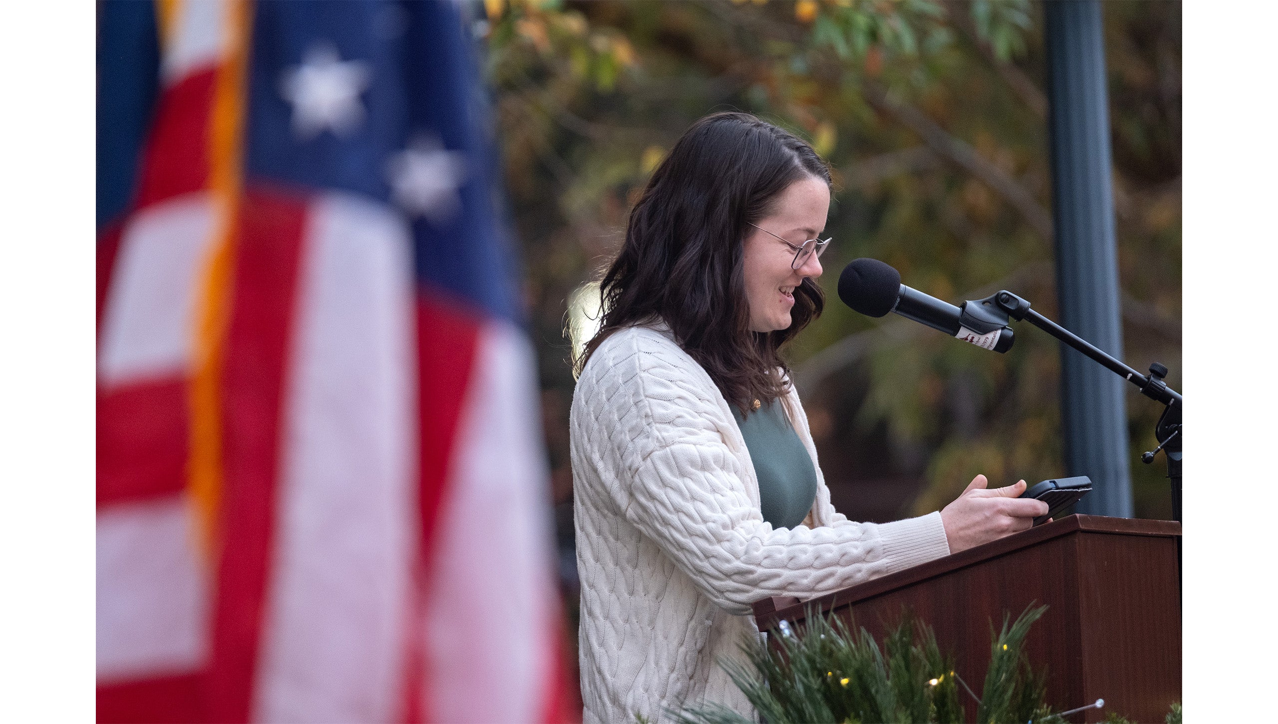 Student Roslyn Ward speaking into a microphone from a podium while looking down at notes on her iPhone at the grand opening of the UNC The Military and Veteran Student Success Center.