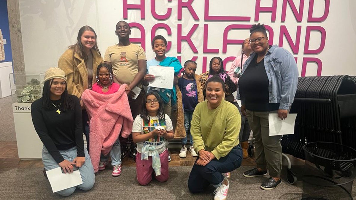 Group of elementary-aged children and adult volunteers posing for a group photo at an art museum.