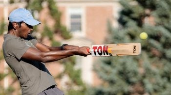 Close-up image of a UNC-Chapel Hill student on Hooker Fields swinging a cricket bat and preparing to make contact with the ball.