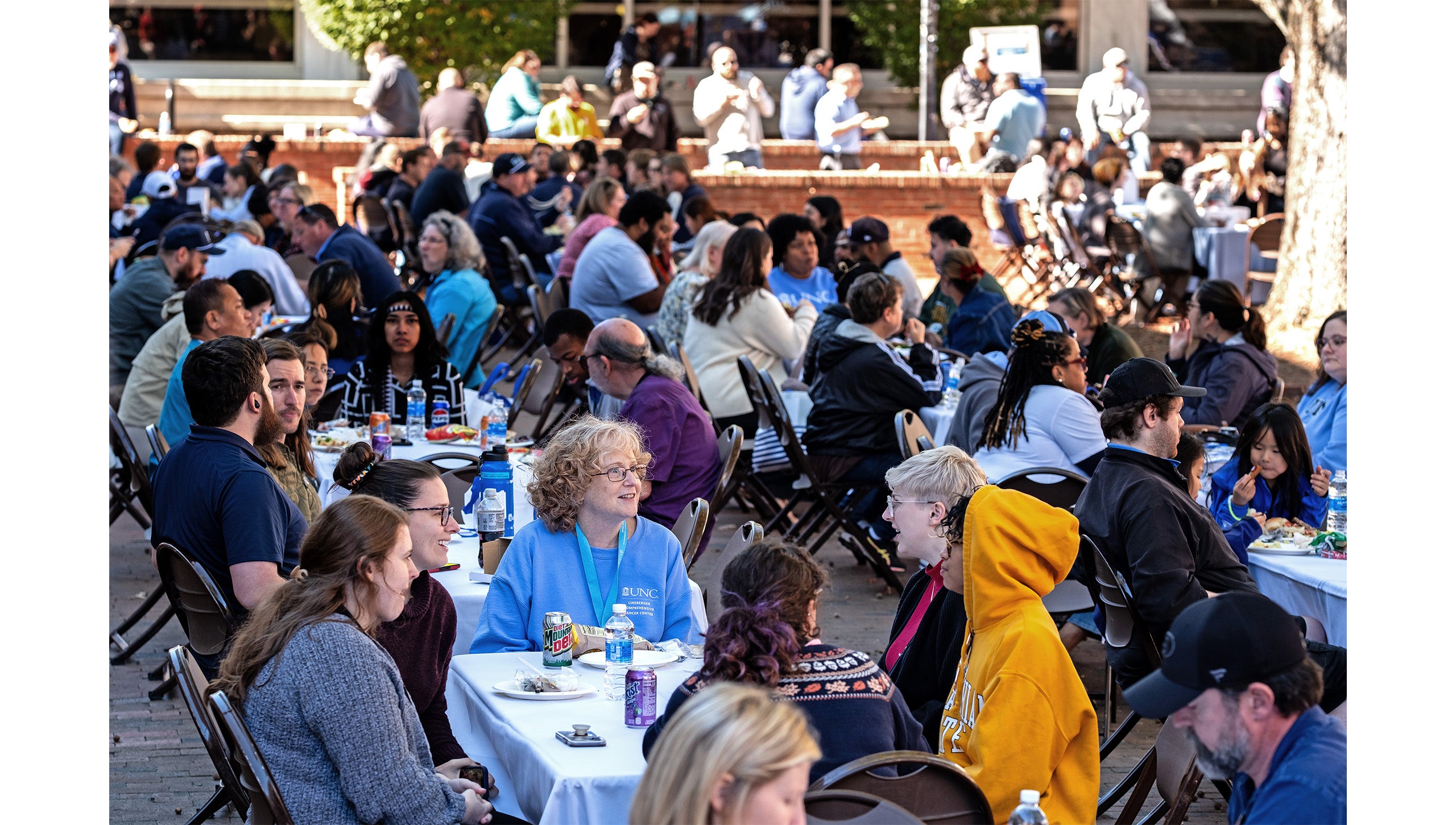 Close-angle shot of many UNC-Chapel Hill employees eating lunch at tables set up in the Pit in front of Student Stores on a sunny day.