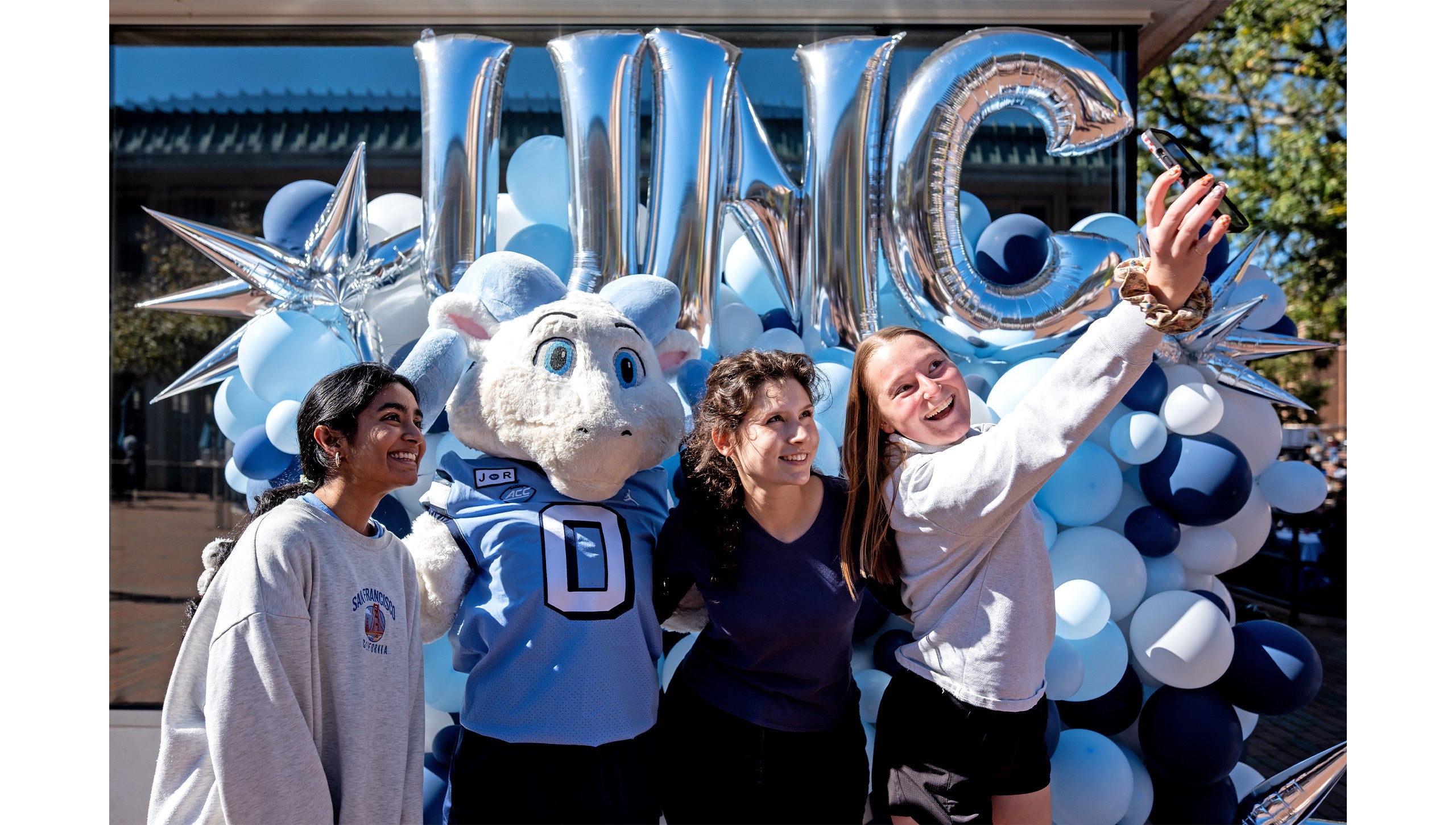 Three UNC-Chapel Hill employees taking a selife with Rameses Jr., one of Carolina's ram mascots.