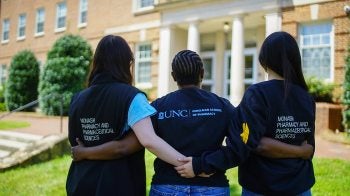 Three students stand together facing the Eshelman School of Pharmacy building. They are wearing T-shirts that say Eshelman or Monash University.
