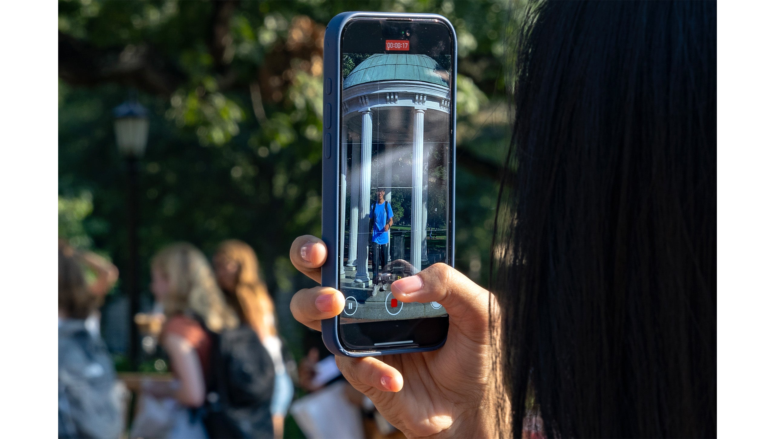 Close-up image of a hand holding an iPhone vertically that's recording video of a UNC-Chapel Hill student taking a sip from the Old Well.