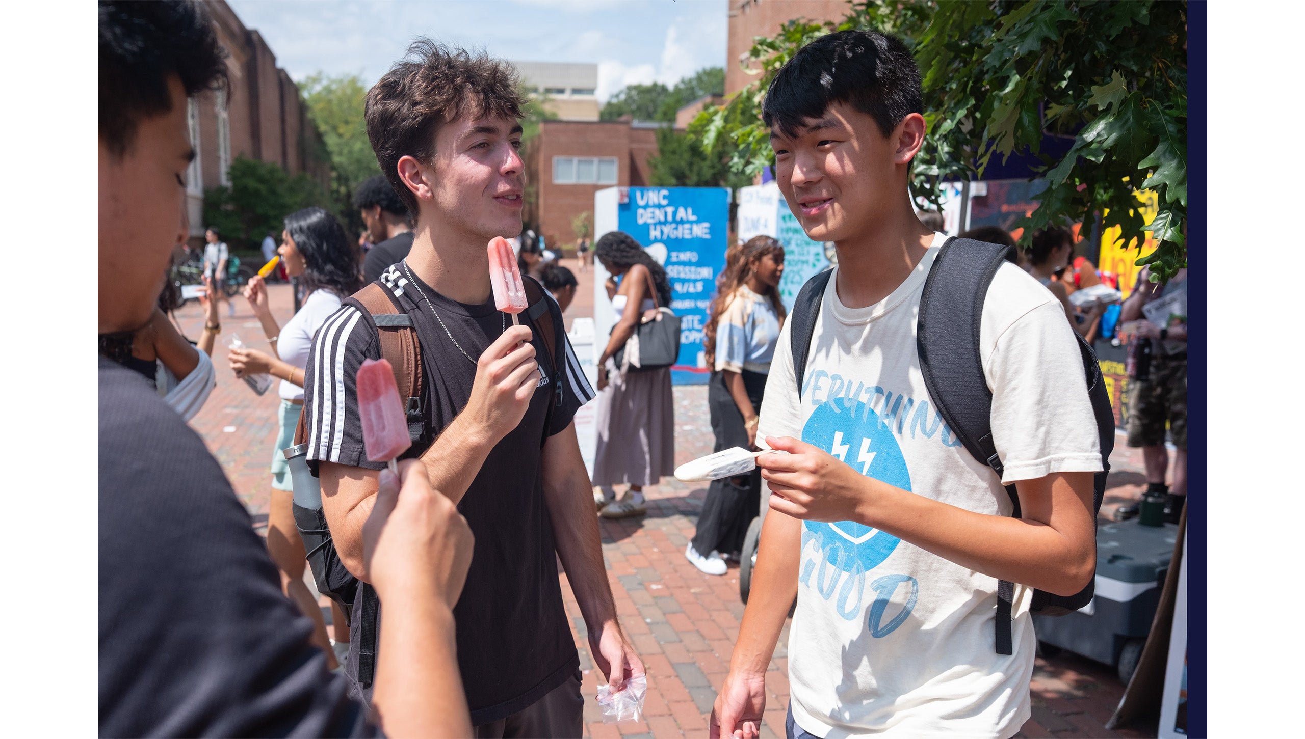Three UNC-Chapel Hill students talking to each other while standing near the Pit and eating LocoPops.
