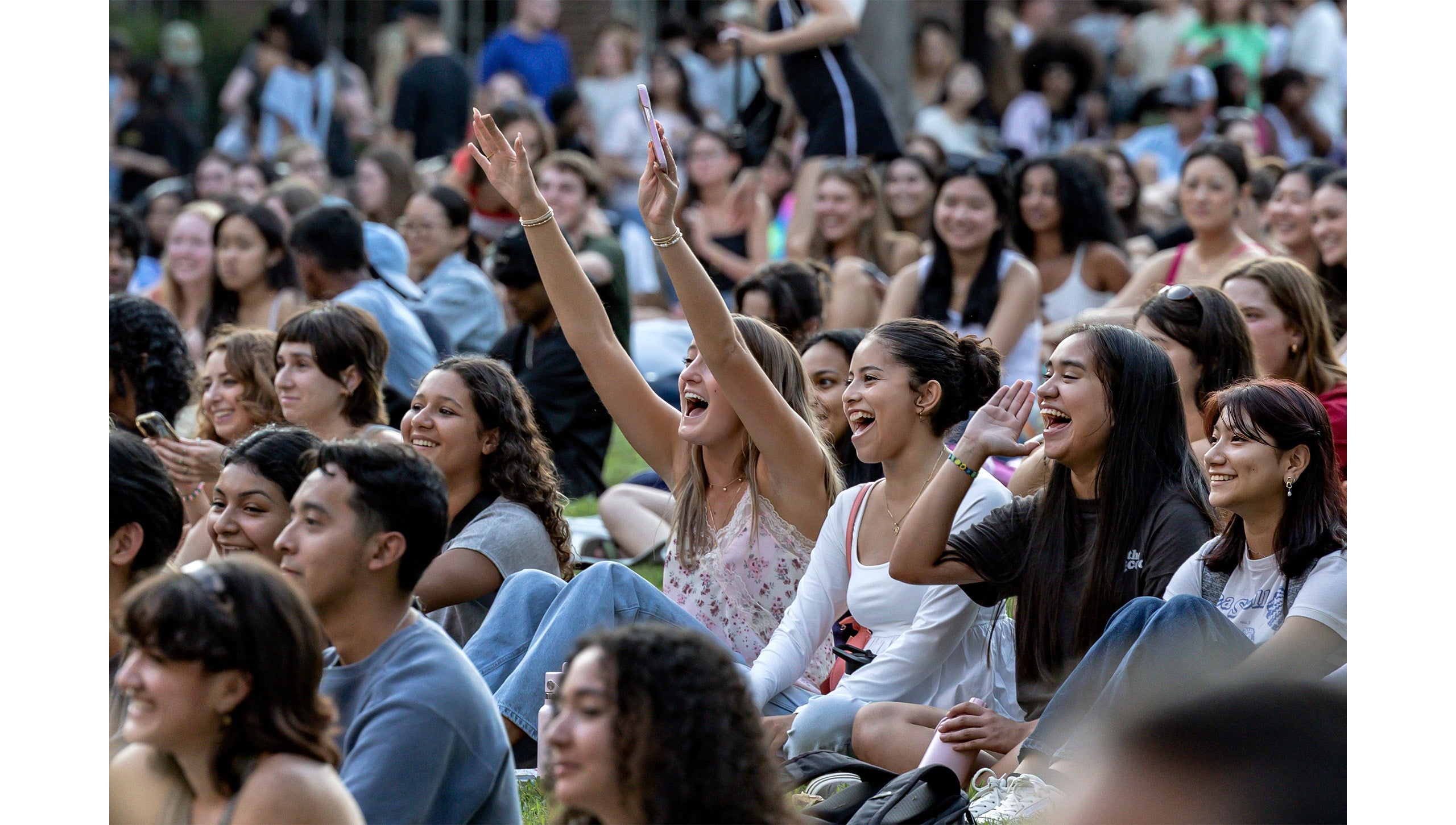 Students sitting on the lawn of Polk Place and cheering on fellwo student a cappella group performers at Sunset Serenade.