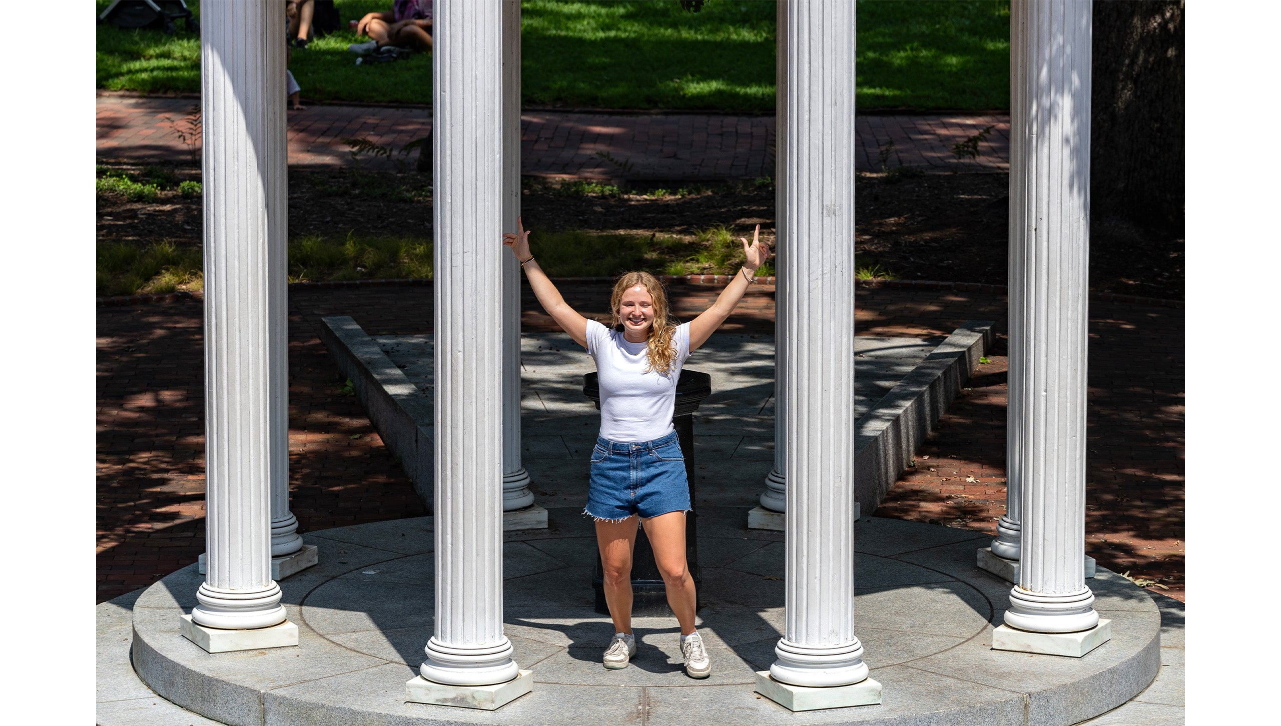 Student posing for photo in front of the fountain of the Old Well on the campus of UNC-Chapel Hill.
