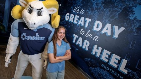 A UNC-Chapel Hill student, Gillian Kepley, posing for a photo while leaning up against a Rameses mascot on display at the UNC Visitors Center.