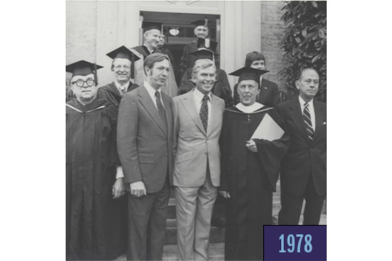 A black-and-white photo of 10 men posing for a photo in front of a University building. In the middle of the first row of men is actor Andy Griffith.