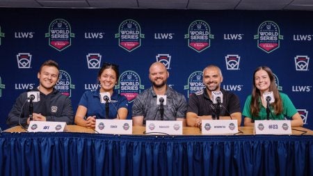 Five Little League World Series employees, including UNC-Chapel Hill student Hannah Smith on the far right, sitting at a news conference table with microphones in front of them.