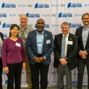 Seven individuals posing in front of sign reading 