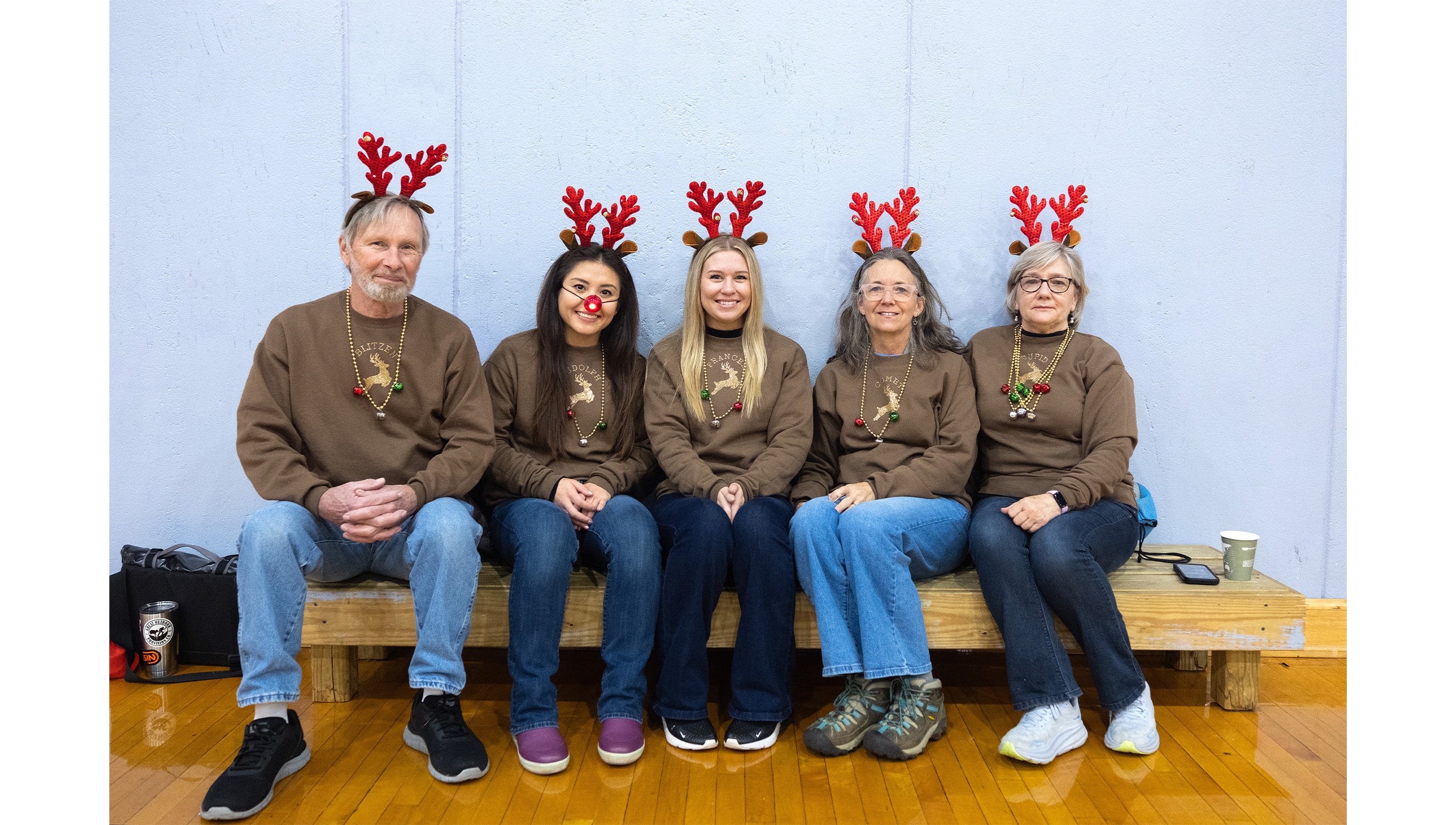 Five UNC-Chapel Hill employees in festive reindeer costumes posing for a group photo inside a gym at Fetzer Hall during the Jingle Bell Jog.