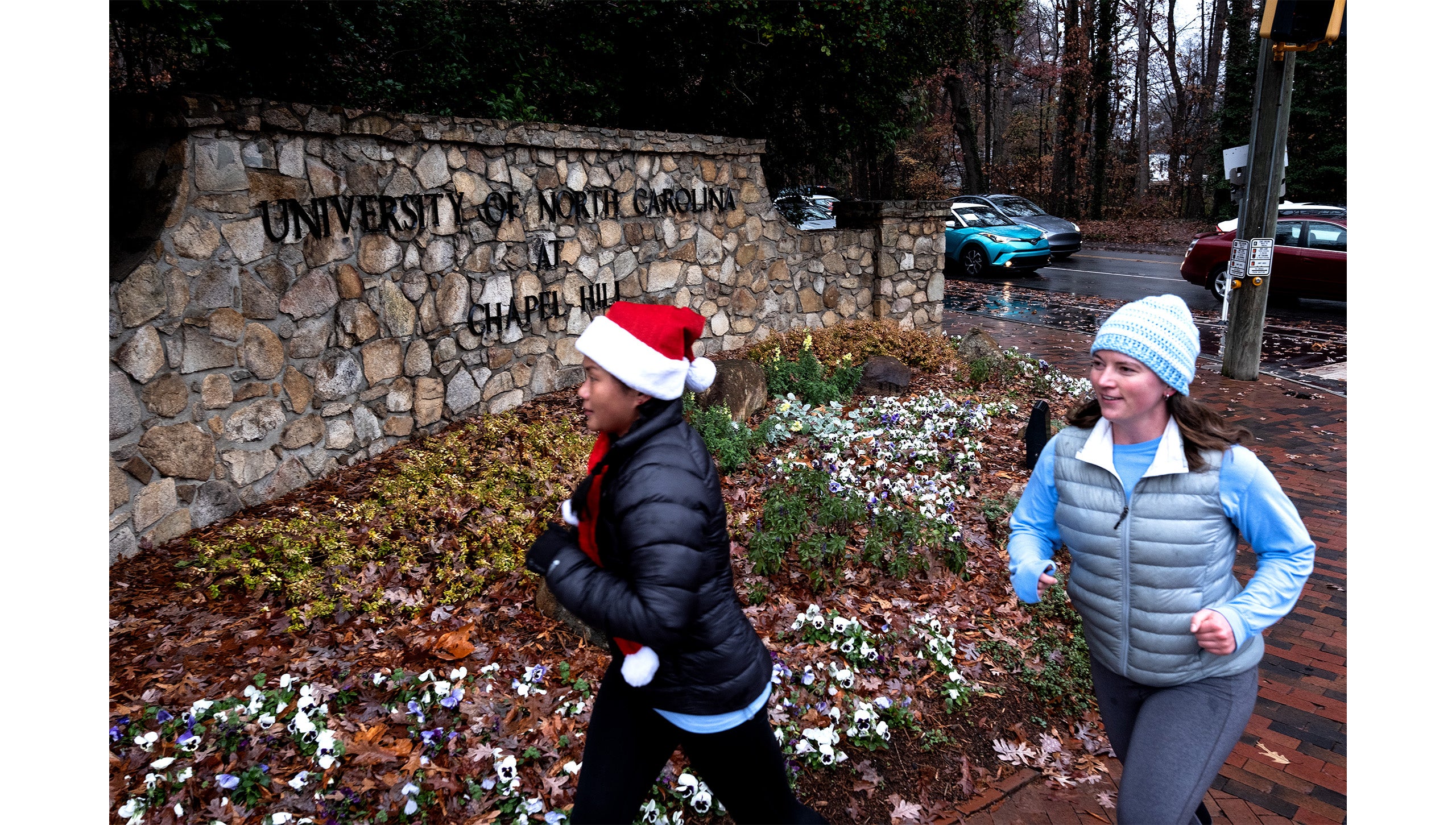 Two UNC-Chapel Hill employees jogging by a stone sign reading 