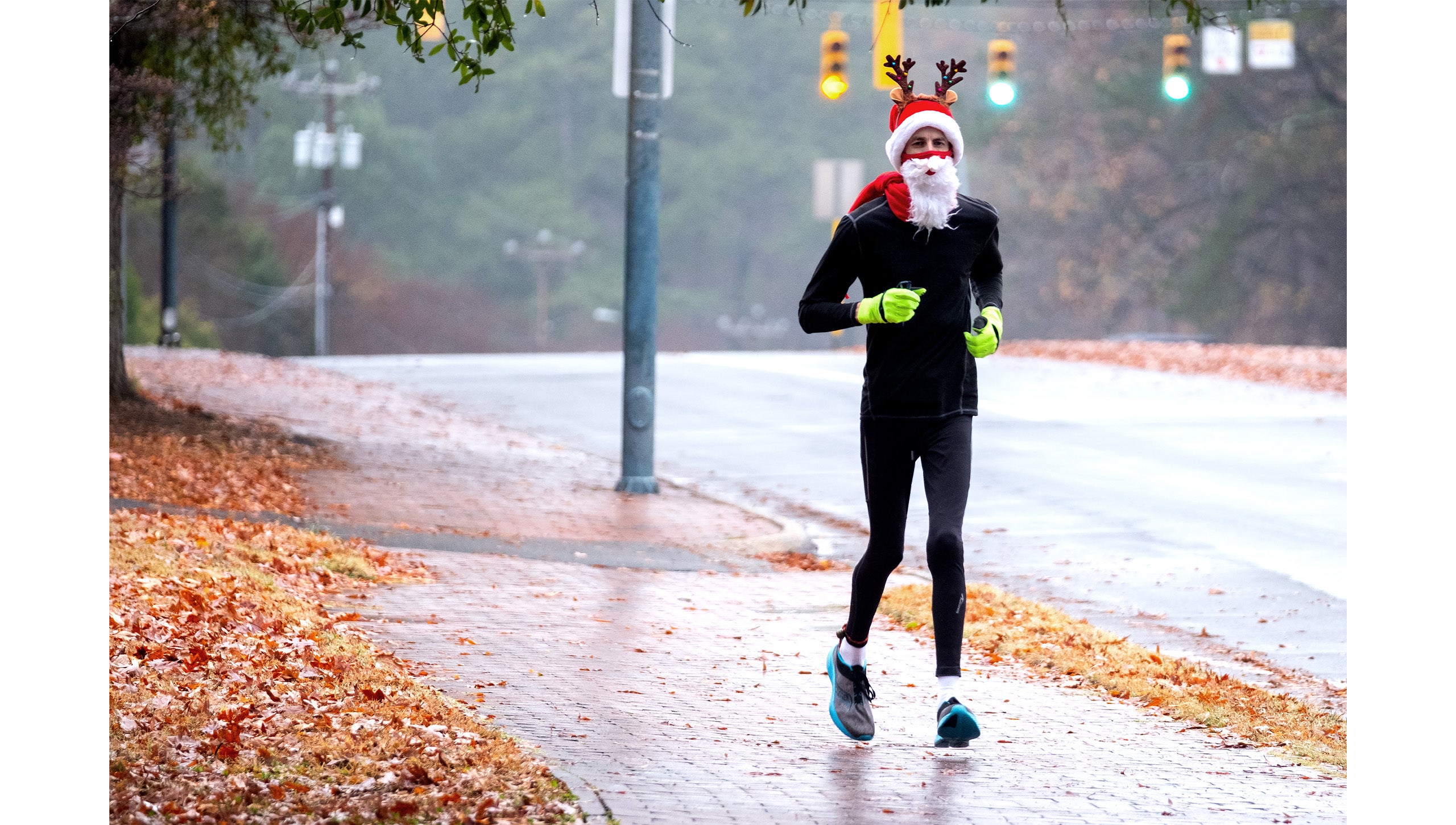 A man wearing a Santa hat and beard and Reindeer ears jogging down a brick sidwalk during the UNC-Chapel Hill Jingle Bell Jog
