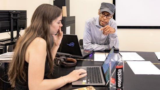 Kerwin Young instructing a student in his beat making course as she looks at her laptop.