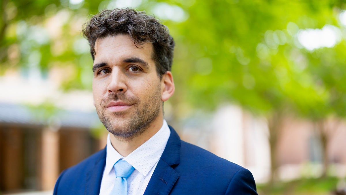 Frank Leibfarth posing for portrait on campus of UNC-Chapel Hill outside a building near trees.