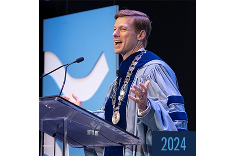 UNC-Chapel Hill Chancellor Lee H. Roberts in Carolina Blue and Navy Blue regalia speaking into a microphone at University Day.