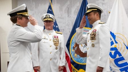 Three individuals in Naval uniforms saluting one another.