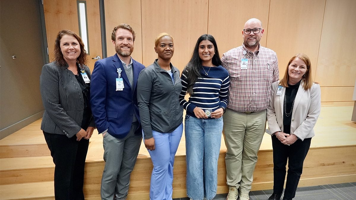 Group of five people from UNC Health's nursing program presenting a student, Neha Varrier, a challenge coin for her efforts in saving a person's life with CPR.