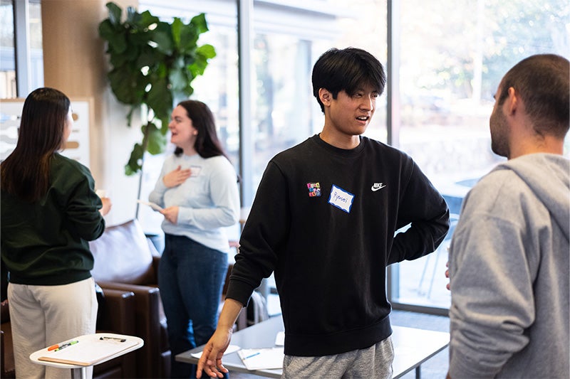 In the foreground, Ryusei Kimura has a conversation with Marcos Eduardo Gomes do Carmo at the Speaking Group. Also pictured in the background are Stacy Thornton and Kokoro Waka having a conversation.