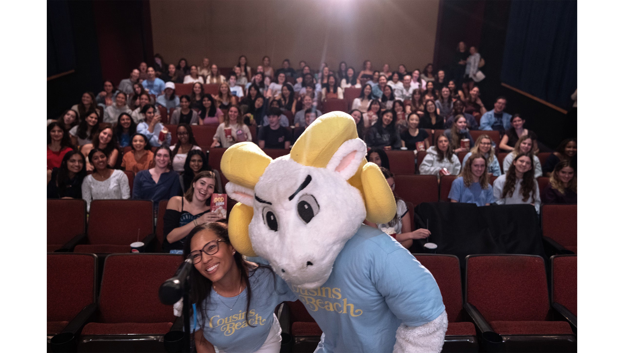 A woman, Rhonda Beatty, taking a photo with Rameses, UNC-Chapel Hill's ram mascot, in front of rows of students at “The Summer I Turned Pretty” watch party at the Varsity Theatre.
