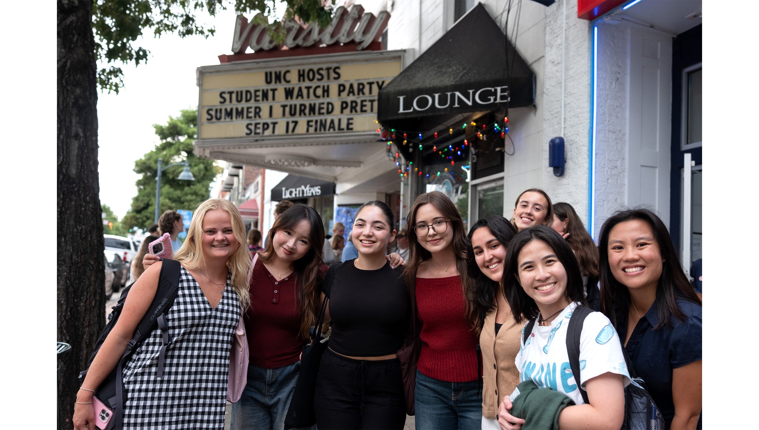 Group of eight UNC-Chapel Hill students posing for a portrait on Franklin Street sidewalk waiting to enter “The Summer I Turned Pretty” watch party at the Varsity Theatre.