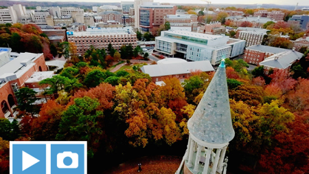 An aerial view of the Bell Tower and U.N.C. Chapel Hill's campus in the fall. The trees have orange and yellow leaves.