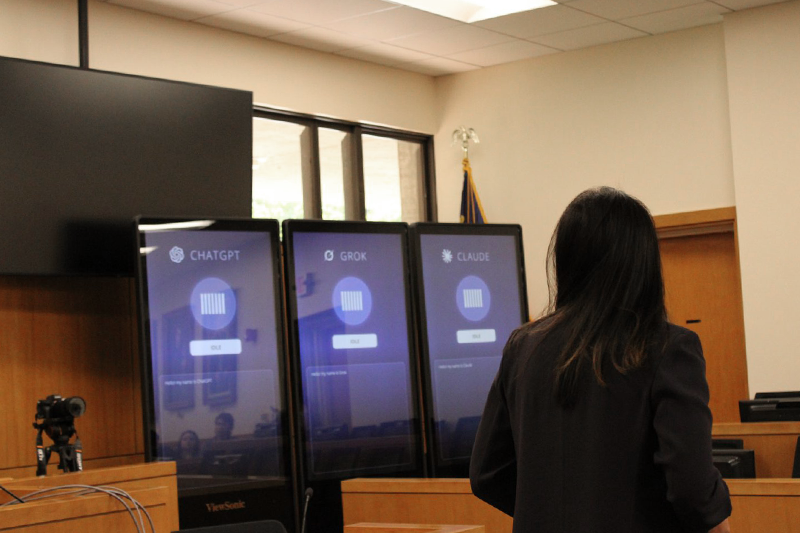 A person standing in front of three screens that represent three different Artificial Intelligence models arguing their case for the mock trial.
