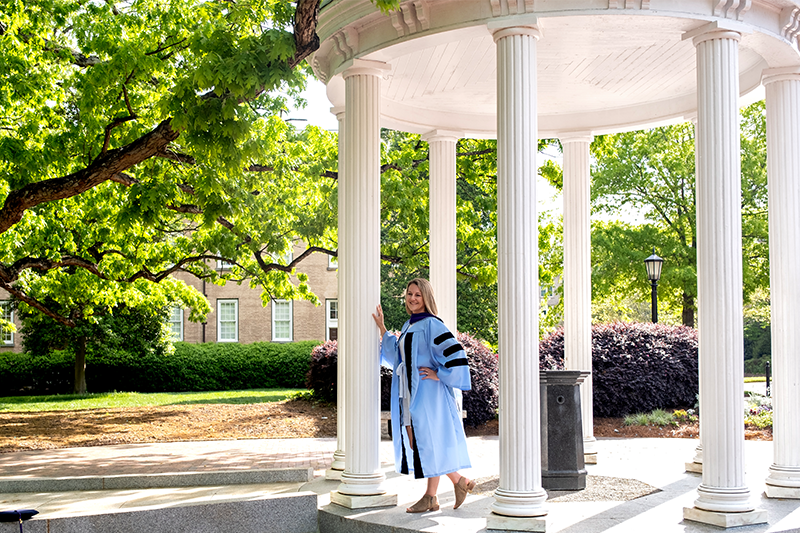 Brittany Anker in her U.N.C. graduation robes poses for a photo at the Old Well.