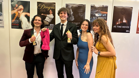 Four students posing with awards statues in front of posters of fellow students' films.