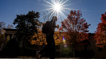 Student walking on campus holding coffee.
