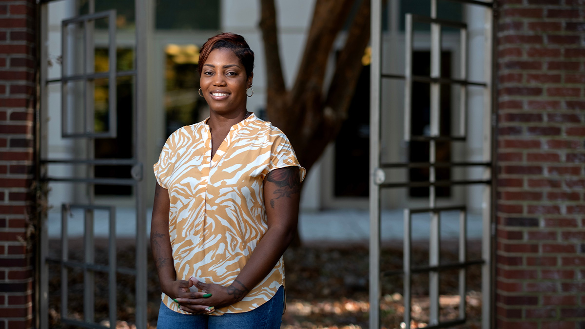 Sheree Stewart poses in front of brick wall and gate.