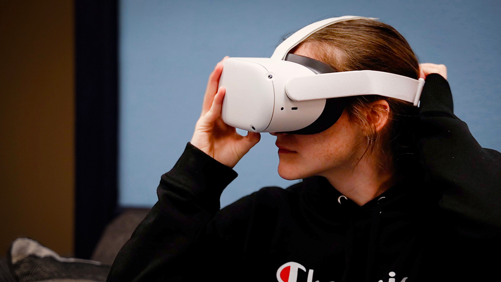 Woman wearing white VR headset in front of Carolina Blue wall.