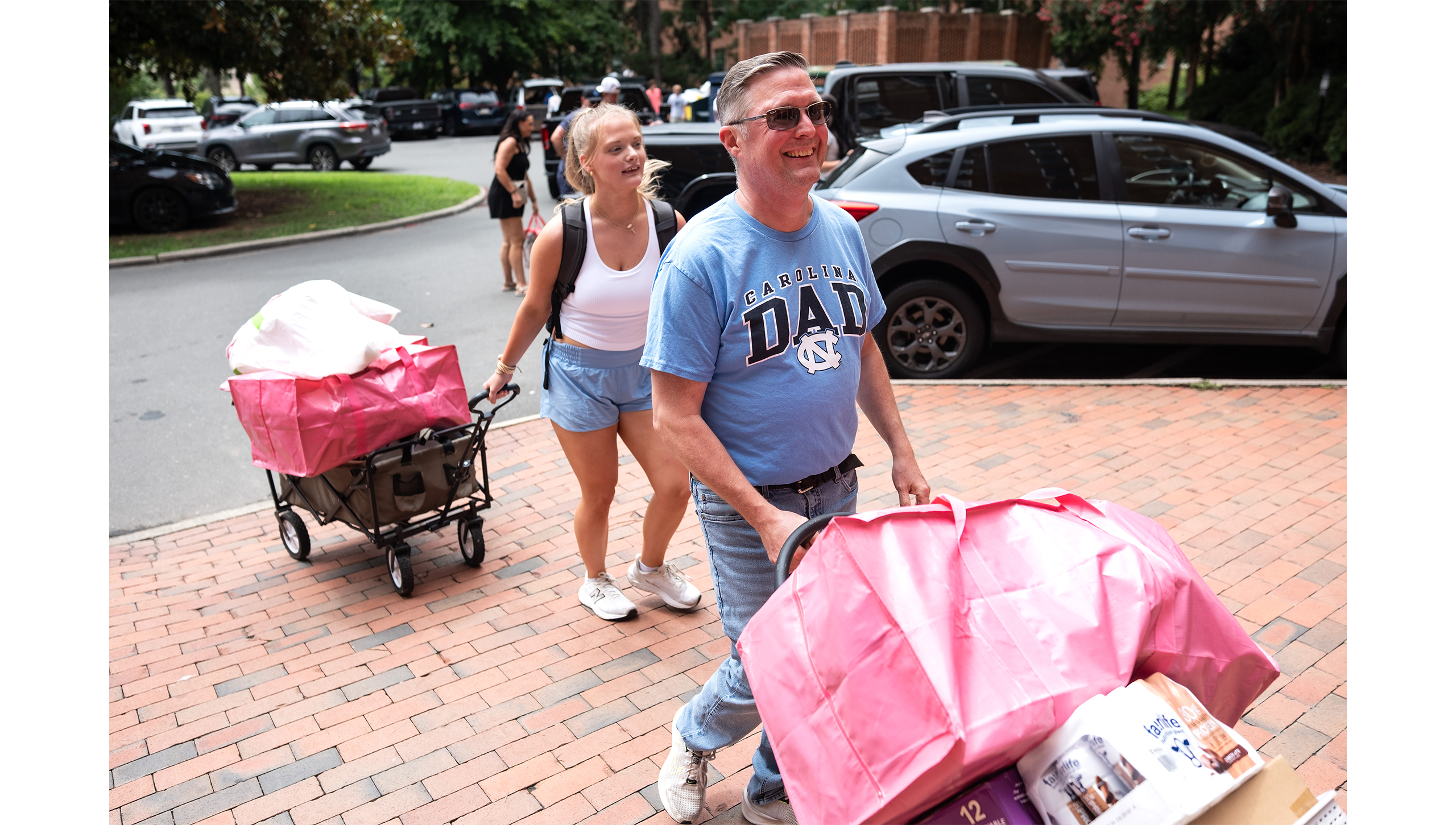 Father and daughter rolling bags of luggage across a parking lot.
