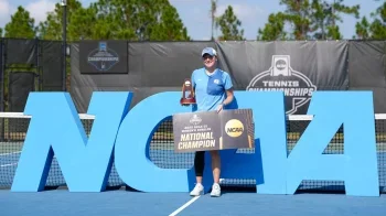 Reese Brantmeier holding her national championship trophy and holding a national champion sign on a tennis court.